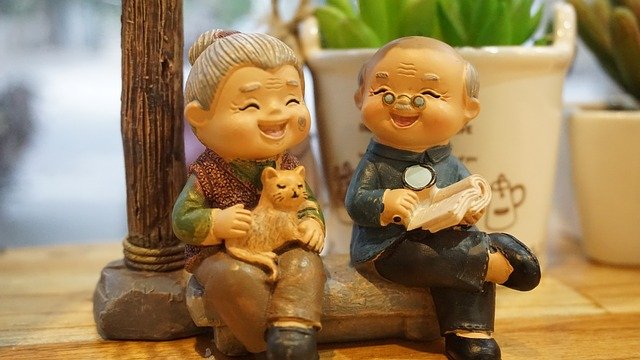 figurines of old lady with a cat and old man with a book, both sitting on a bench and smiling