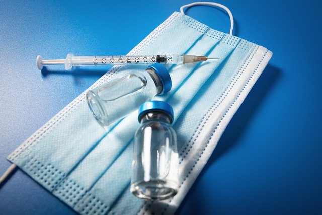 injection viles and syringe with needle sitting on a face mask